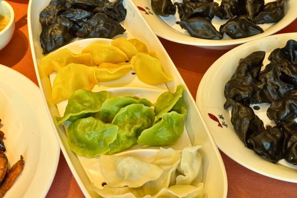 Assortiment de raviolis au maquereau de Qingdao, colorés en jaune, vert, blanc et noir, présentés dans des assiettes de restaurant