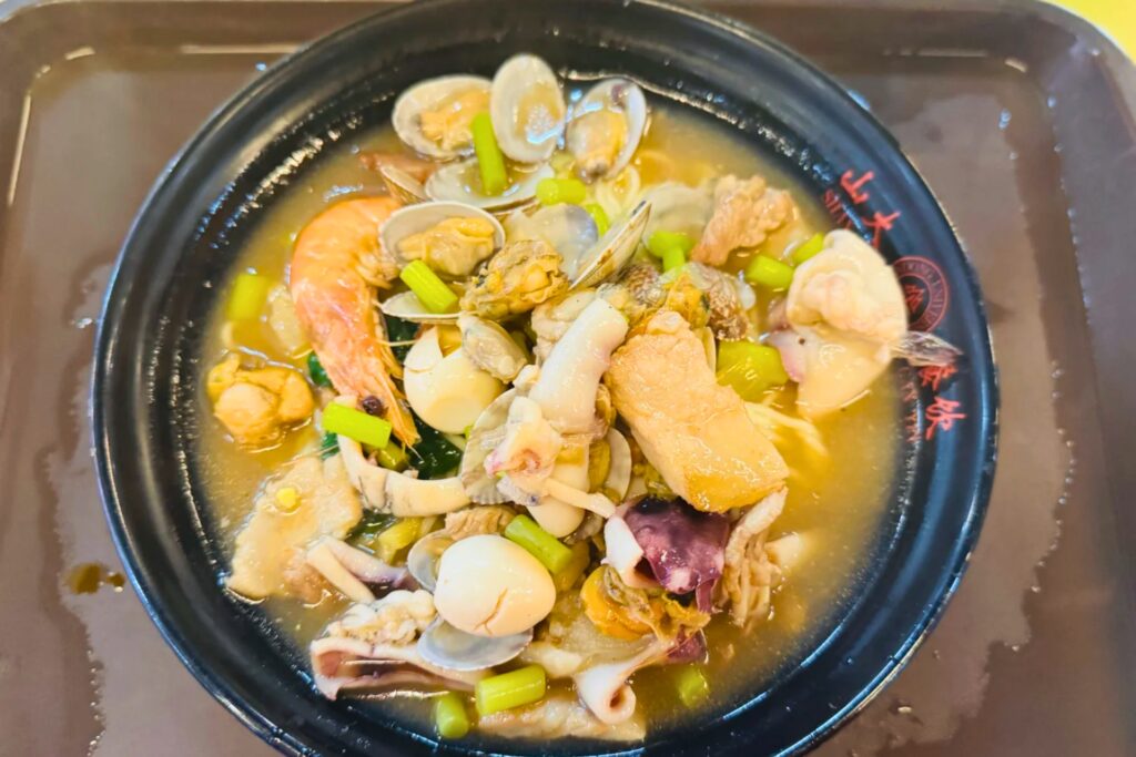 Bol de wontons aux crevettes dans un bouillon clair, garnis de ciboulette ciselée