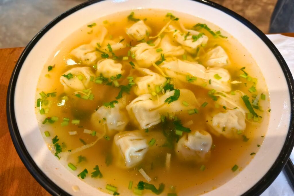Bol de wontons aux crevettes dans un bouillon clair, garnis de ciboulette ciselée