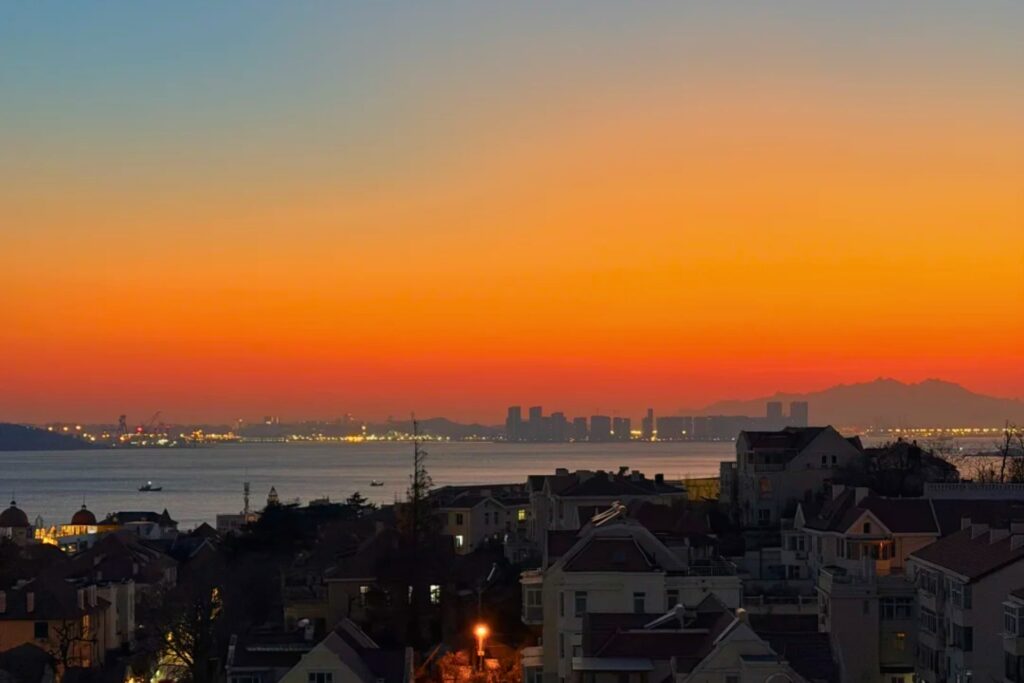 Coucher de soleil orange et rouge sur la baie de Qingdao, vu depuis la colline Xiaoyushan avec les toits de la vieille ville au premier plan