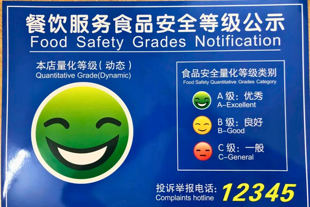 Panneau officiel d'inspection sanitaire (Smiley vert ou jaune) affiché dans un restaurant chinois certifiant un bon niveau d'hygiène