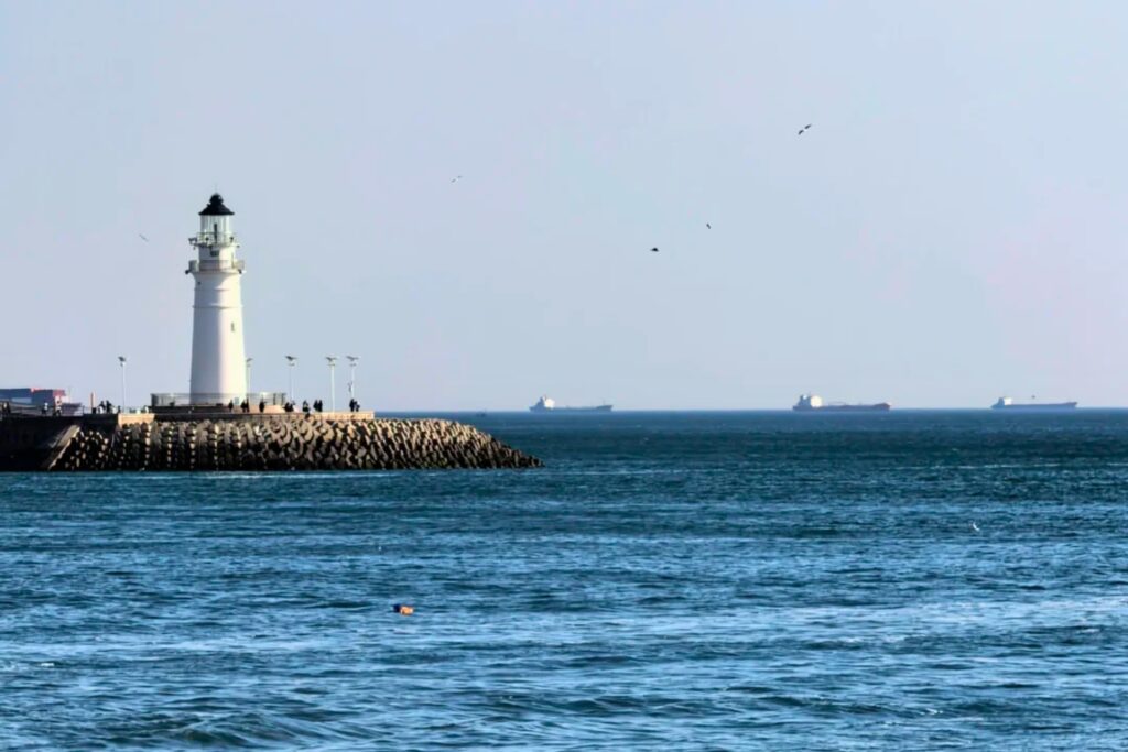 Phare blanc de Xiaoqingdao se dressant sur une jetée rocheuse, entouré par la mer et des bateaux au loin