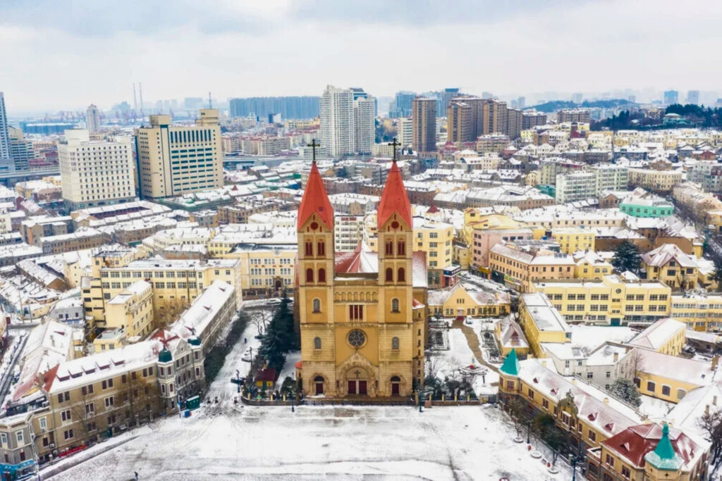 Vue aérienne de la cathédrale Saint-Michel de Qingdao entourée d’immeubles et de toits enneigés en hiver